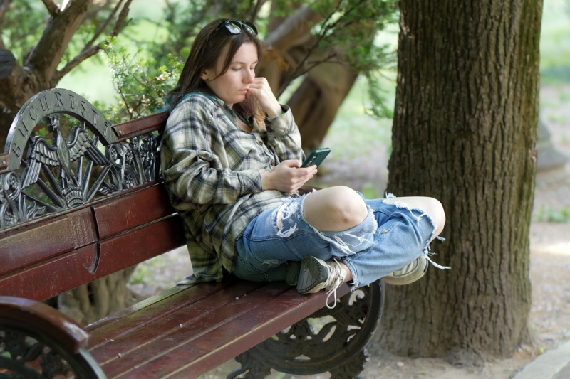 Person sitting on a wooden park bench using a smartphone